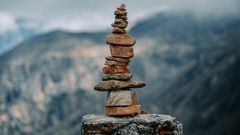 Pierres empilées en équilibre dans un paysage de montagne, illustrant l’apaisement émotionnel et le calme intérieur que permet le chemin de la méthode C.L.A.I.R.E