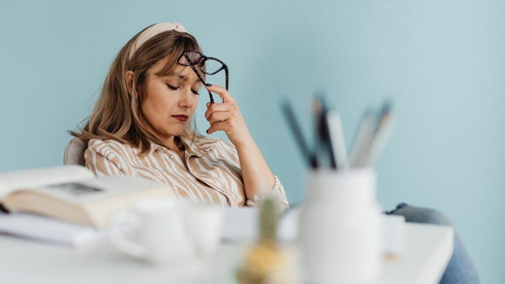 Femme en pleine réflexion tenant ses lunettes, illustrant l’étape Comprendre de la méthode C.L.A.I.R.E de consultation libération émotionnelle